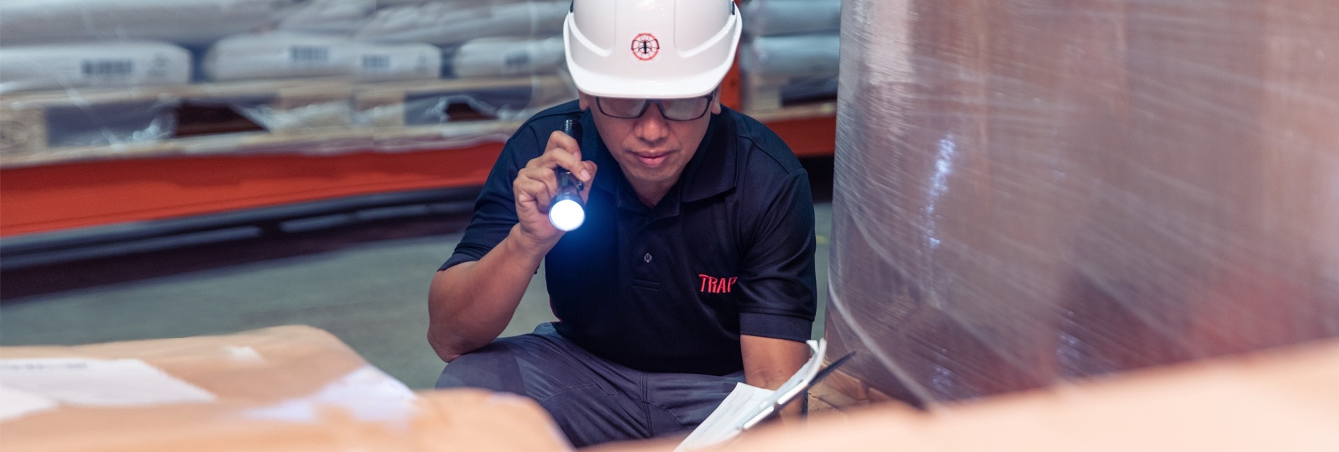 A TRAP pest control employee holding a flashlight inspecting a factory