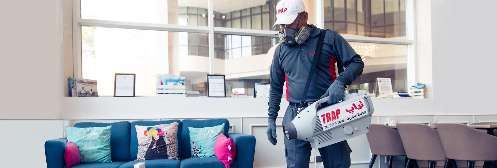 A TRAP pest control expert wearing a mask disinfecting a living room using a special tool